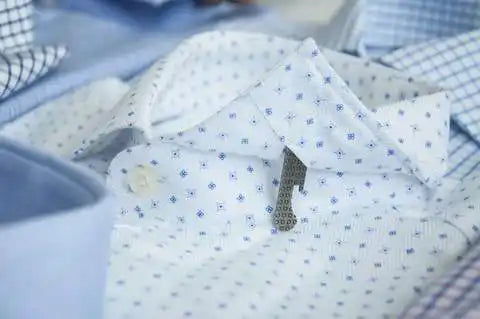 Camisa blanca de vestir con pequeños lunares azules y un stay de cuello visible.