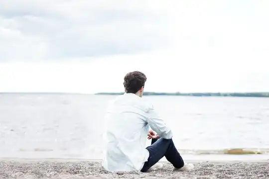 Alguien con una camisa blanca sentado solo en una playa.