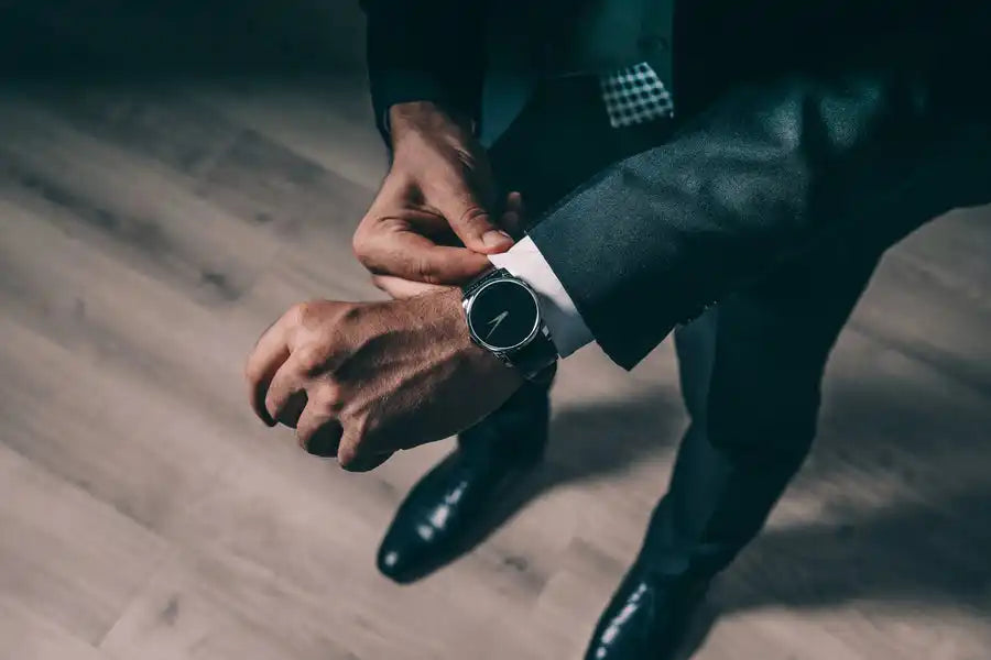 Manos ajustando un elegante reloj de pulsera mientras llevan un traje oscuro.