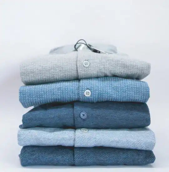 Montón de camisas abotonadas azules y grises dobladas ordenadamente.